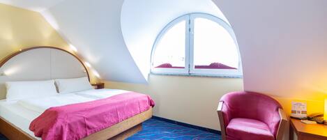 A hotel room with a bed, a chair, a desk, and a large window.