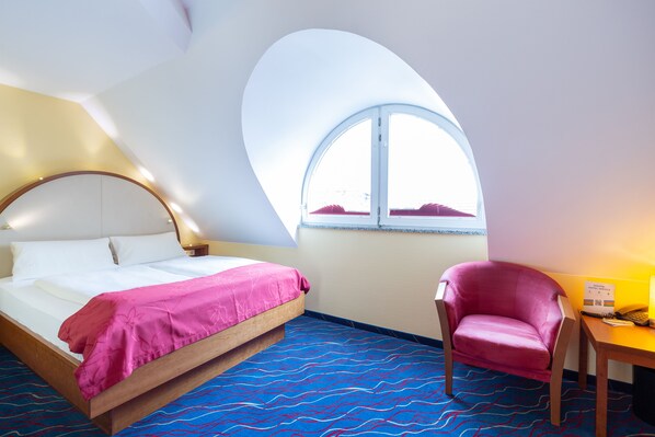 A hotel room with a bed, a chair, a desk, and a large window.