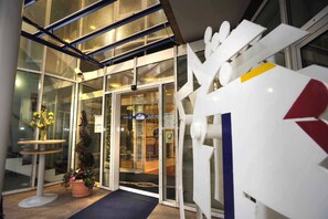 A hotel entrance with a glass door, a potted plant, and a white sign with a red arrow. - Hotel am Schillerpark (Esslingen)