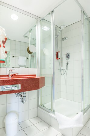 A modern bathroom with a glass-enclosed shower, a white bathtub, and a red-tiled vanity. - Hotel am Schillerpark (Esslingen)