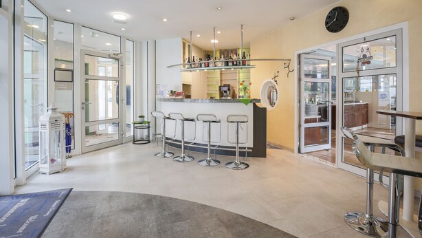 A modern kitchen with a bar area, bar stools, and a clock on the wall. - Hotel am Schillerpark (Esslingen)