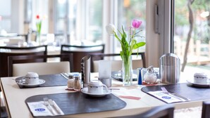 A dining table set with a teapot, cups, and a vase with flowers. - Hotel am Schillerpark (Esslingen)