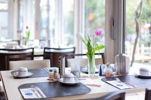 Una mesa de comedor con tetera, tazas y un florero con flores.