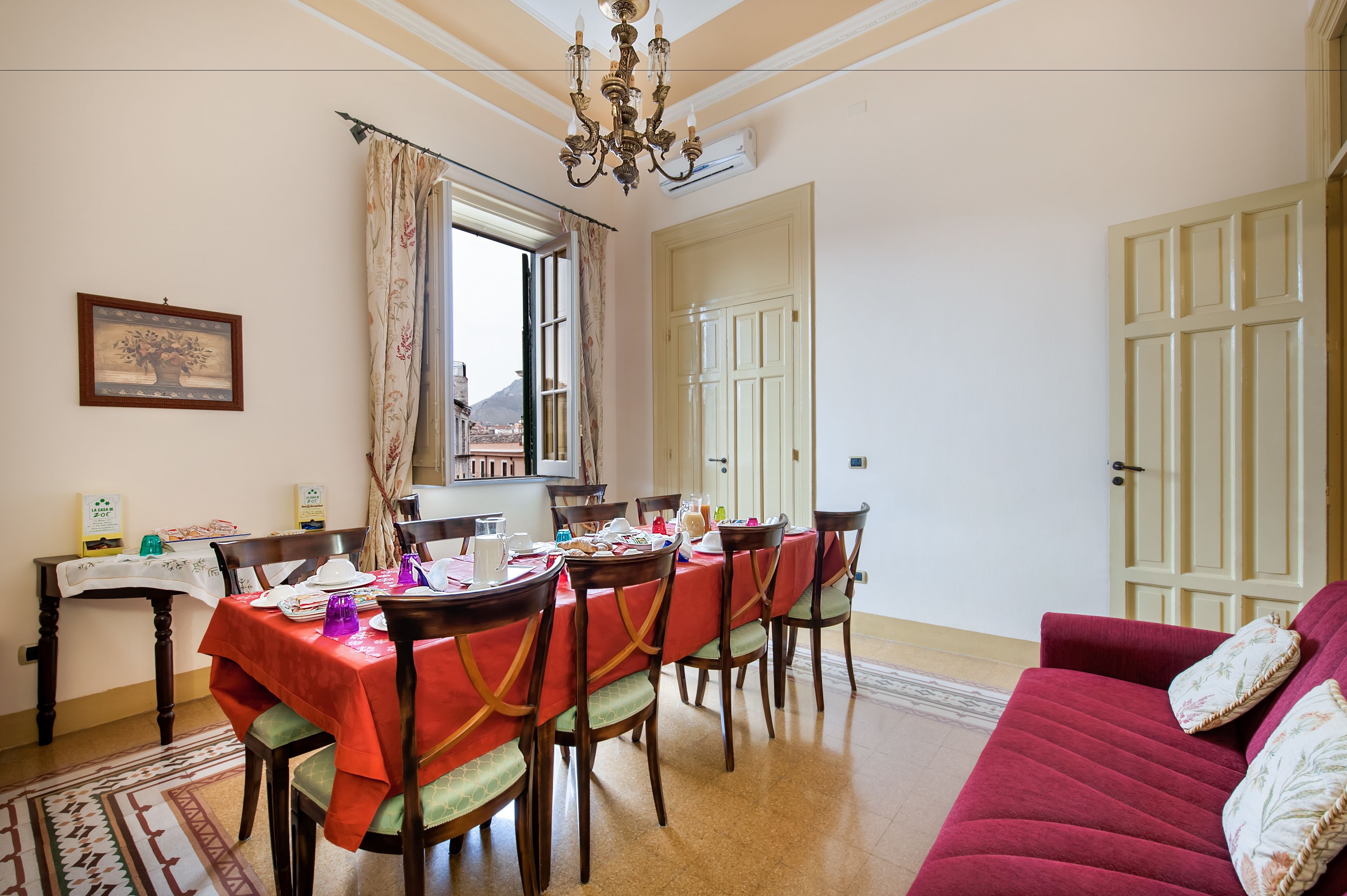 Un coin repas avec une table dressée pour six personnes, une nappe rouge, des chaises en bois et un lustre.