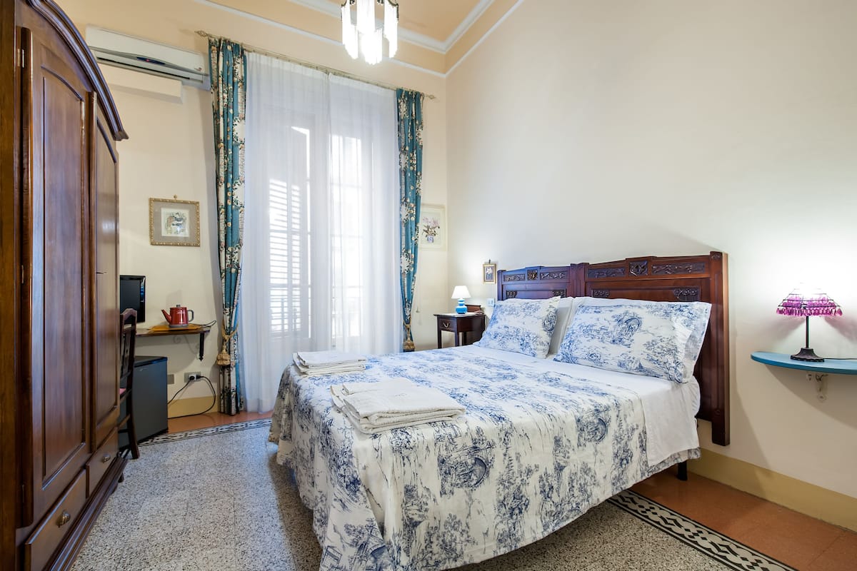 A bedroom with a bed, a nightstand, a lamp, a wardrobe, and a window with curtains.