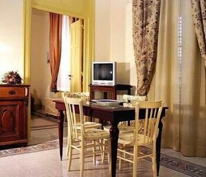 A dining area with a wooden table, four chairs, a television on a stand, and curtains. - La Casa di Zoe (Palermo)