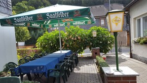 An outdoor seating area with a table covered by a green umbrella labeled "Saalfelder," surrounded by green chairs. - Hotel Gasthaus Steiger (Graefenthal)