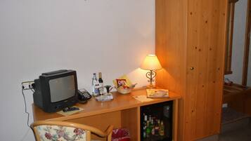 A small room with a wooden desk, a television, a lamp, and a mini-fridge.