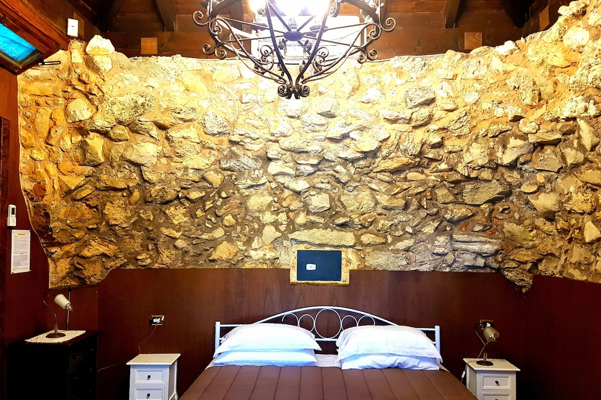 Ein Zimmer mit einer Steinwand, einem Bett mit weißer Bettwäsche, zwei Nachttischen und einer Chandelüster.