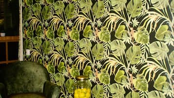 Una habitación con papel tapiz estampado, dos sillones, una mesita con un tarro de limones y suelo de madera.
