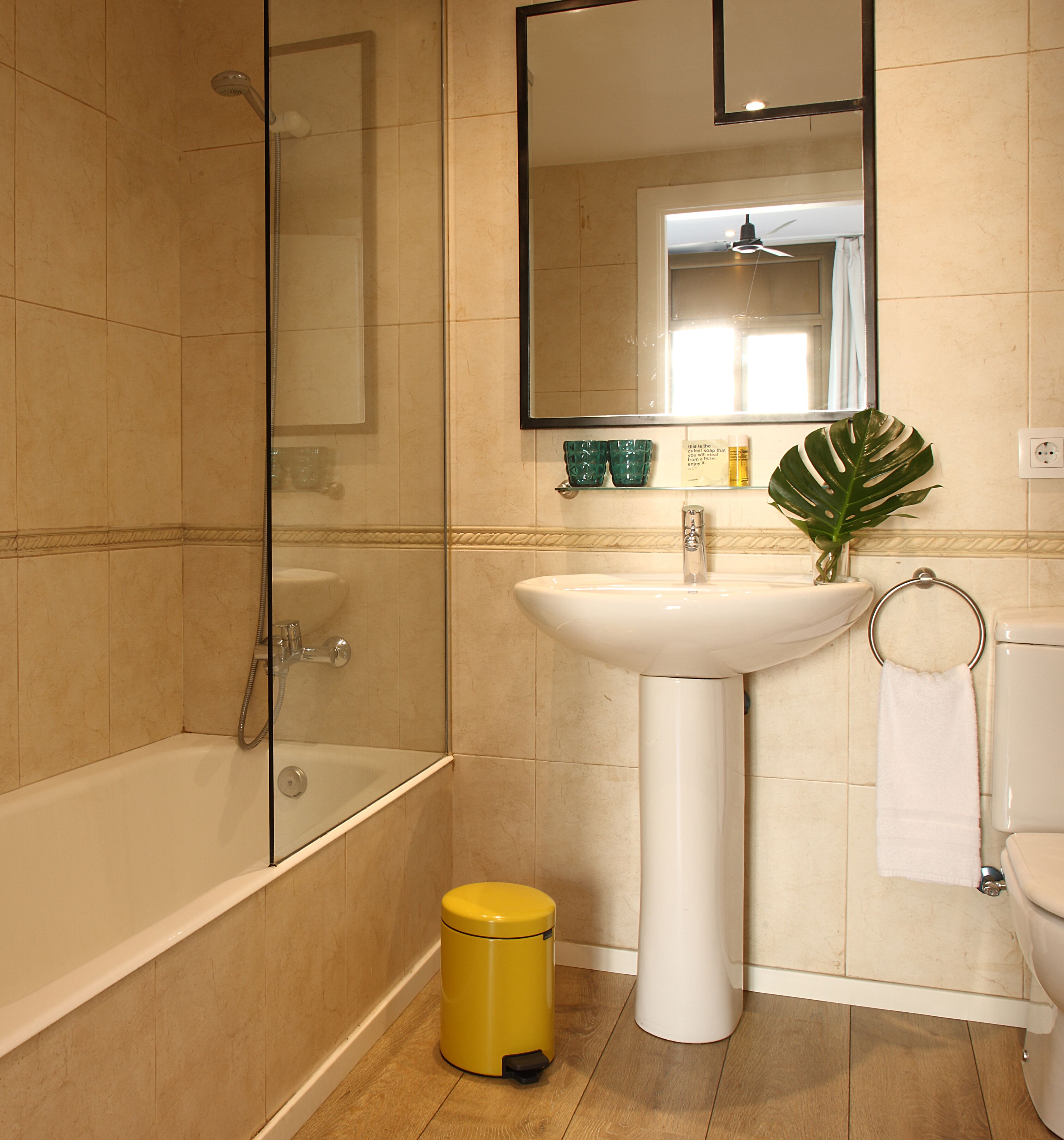 A bathroom with a bathtub, sink, and toilet. There is a yellow trash bin and a green plant on the sink.