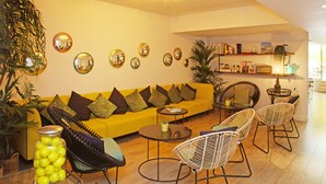 A modern living room with a yellow sofa, wicker chairs, a glass coffee table, and a plant. - chic&basic Lemon Boutique Hotel (Barcelona)