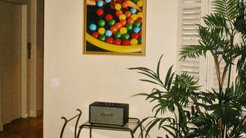 A room with a framed painting, a table with magazines, a radio, and a potted plant.