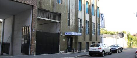 A hotel with a modern facade, a visible entrance, and a parking area with cars.
