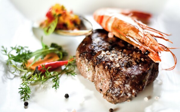A steak with a shrimp on top, garnished with herbs and peppercorns.