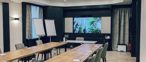 Ett konferensrum med ett långt bord, stolar, en whiteboard, en projektorduk och ett stort fönster med gardiner.