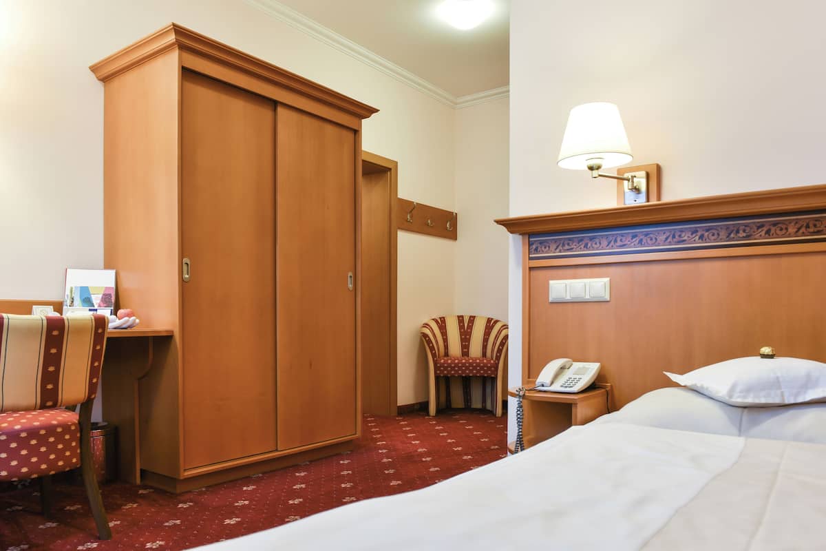 A hotel room with a bed, a desk with a chair, a wardrobe, a telephone, and a lamp.