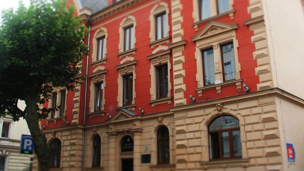 A red and beige building with multiple windows and a tree in front.