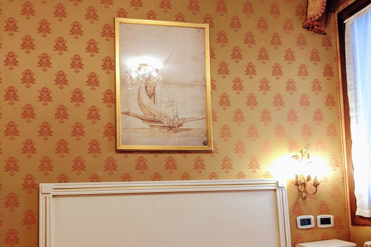 A hotel room with a bed, a wall-mounted painting, a nightstand, and a lamp.