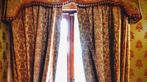 Une fenêtre ornée de rideaux décoratifs et dotée d’un cadre en bois, située dans une pièce dont les murs sont recouverts d’un papier peint à motifs.