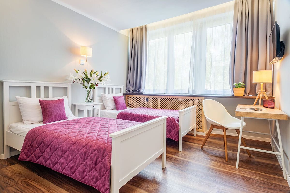 A hotel room with two beds, a desk, a chair, and a window with curtains.
