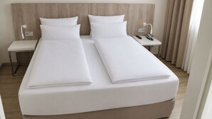 A double bed with white linens, a bedside table with a phone, and a nightstand with a lamp.