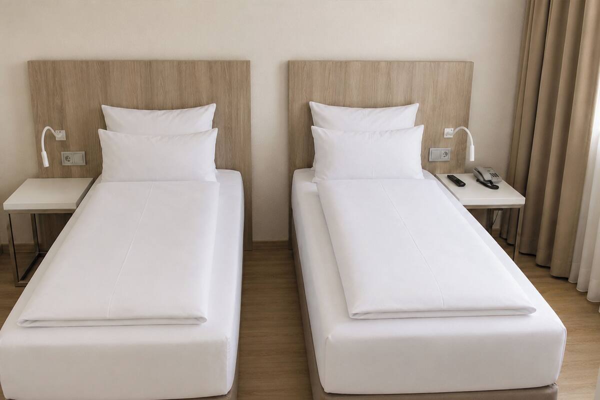 Two single beds with wooden headboards, white bedding, bedside tables with lamps, and a telephone.