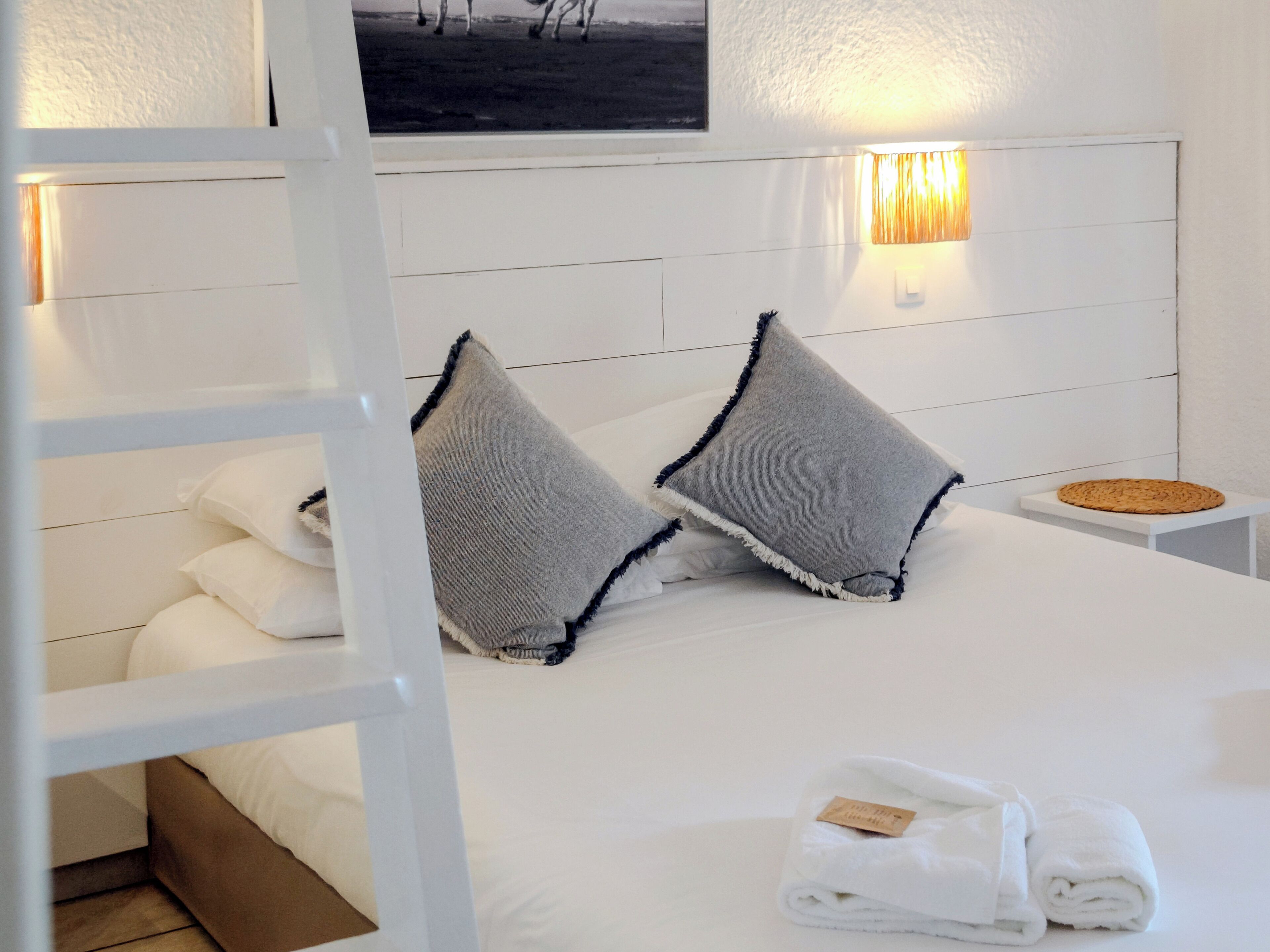 A neatly made bed with pillows, a bedside lamp, and a folded towel on a white nightstand.