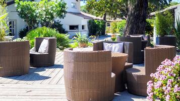 Muebles de mimbre en una terraza de madera con un edificio al fondo.