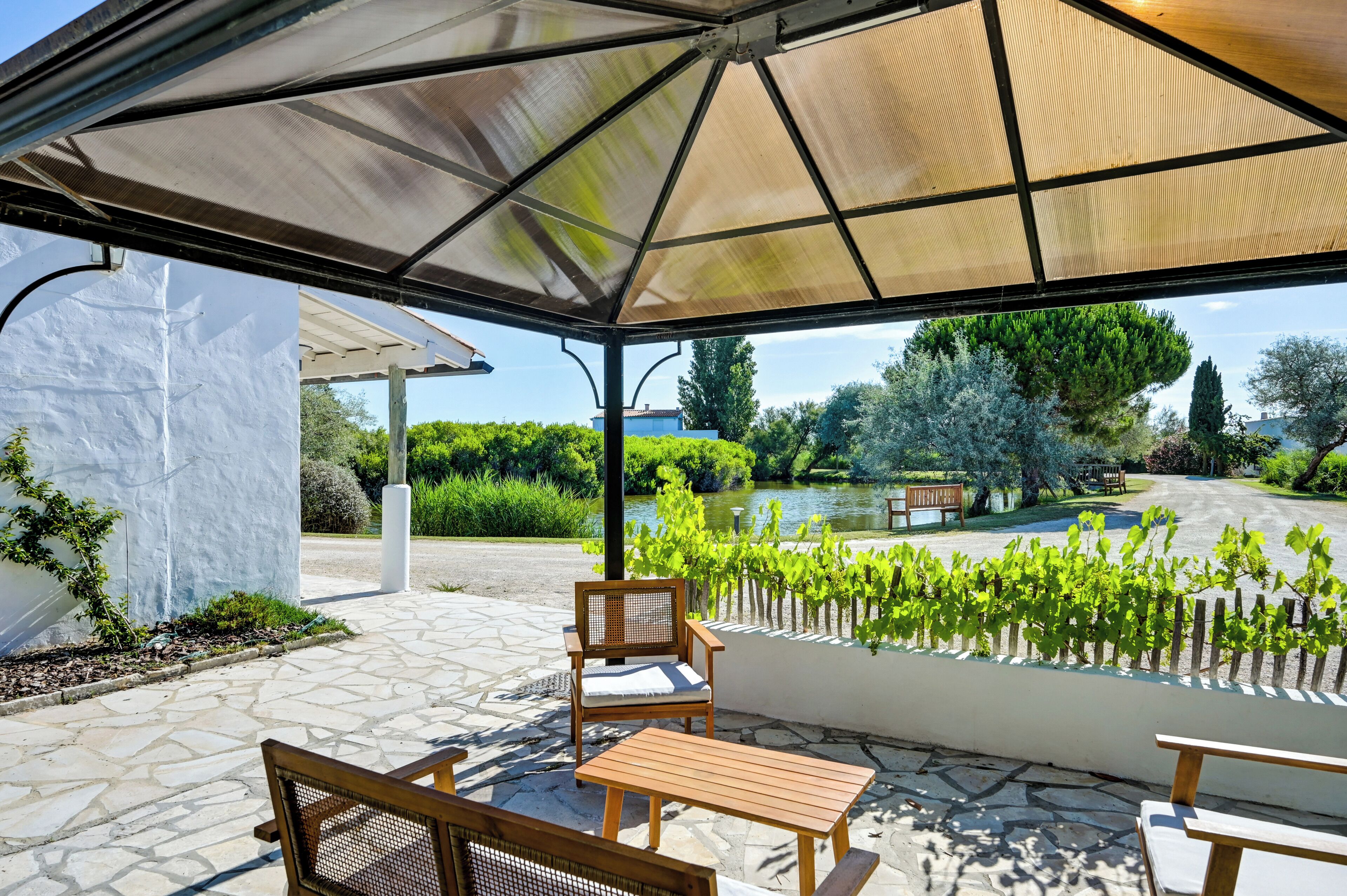 Un'area salotto esterna riparata con tavolo e sedie, una pergola e vista su un giardino e un lago.