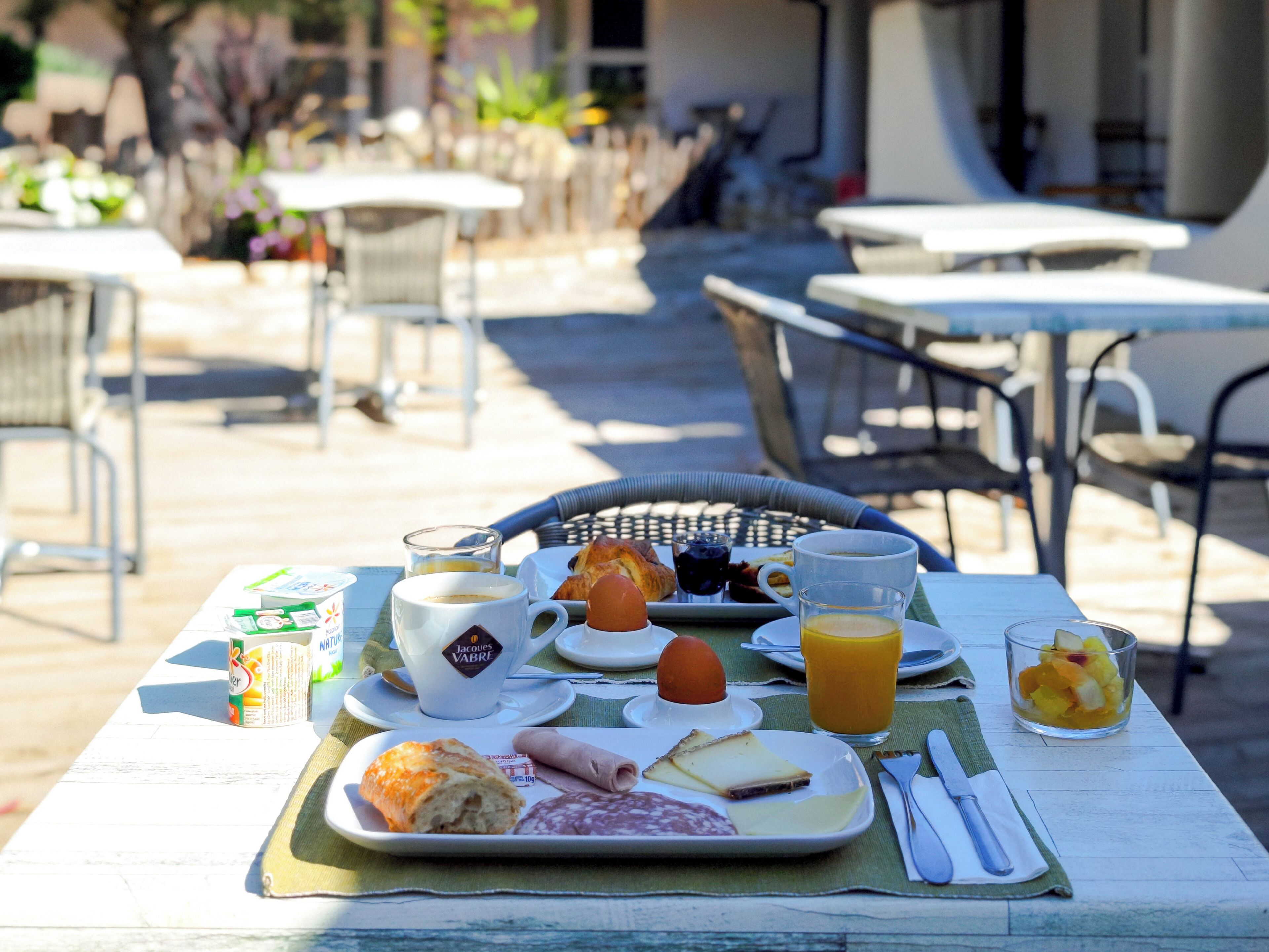 An outdoor dining area with tables, chairs, and a variety of breakfast items including bread, cheese, and fruit.