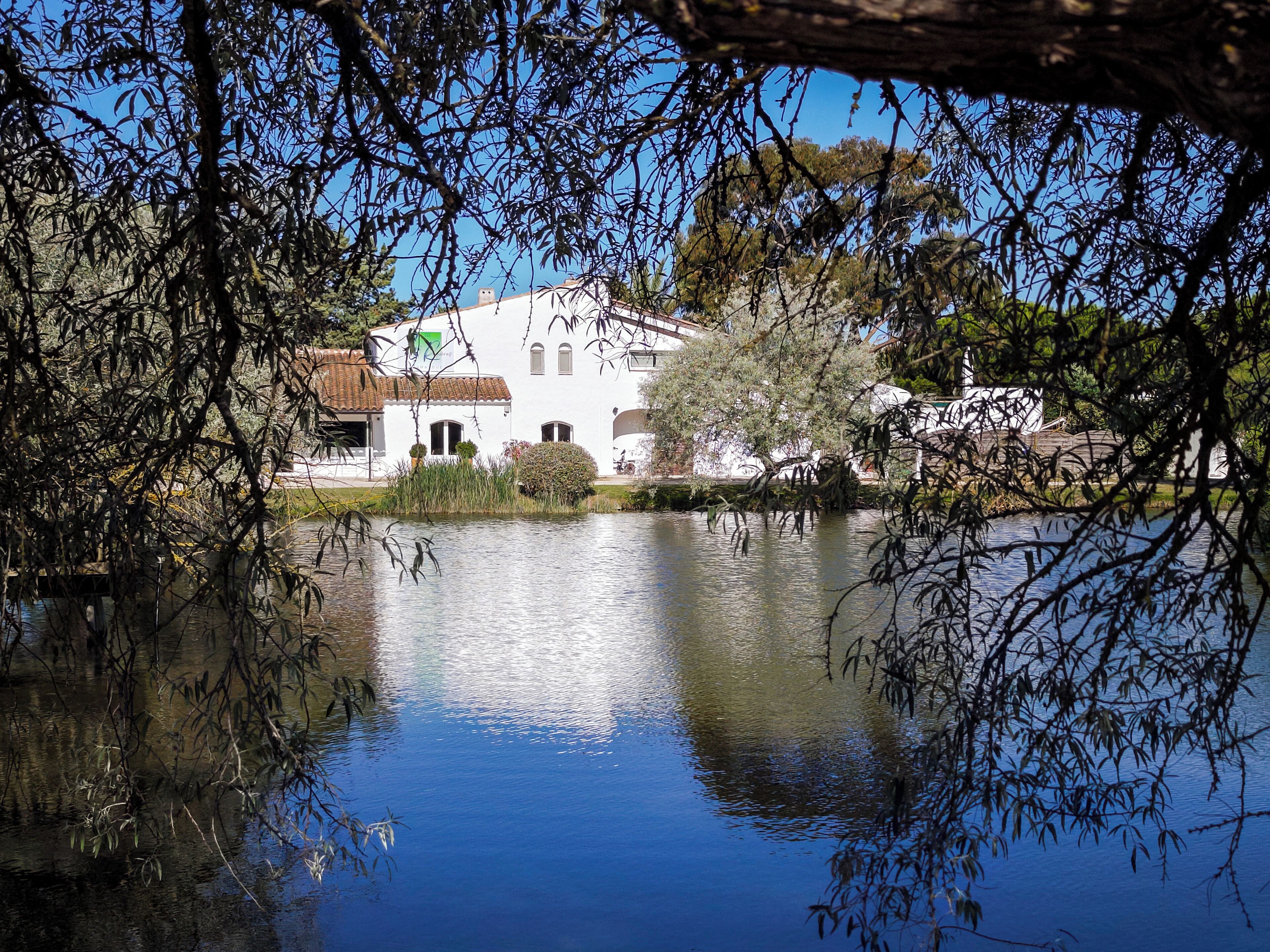 Un edificio blanco con techo de tejas, rodeado por aguas tranquilas y vegetación.