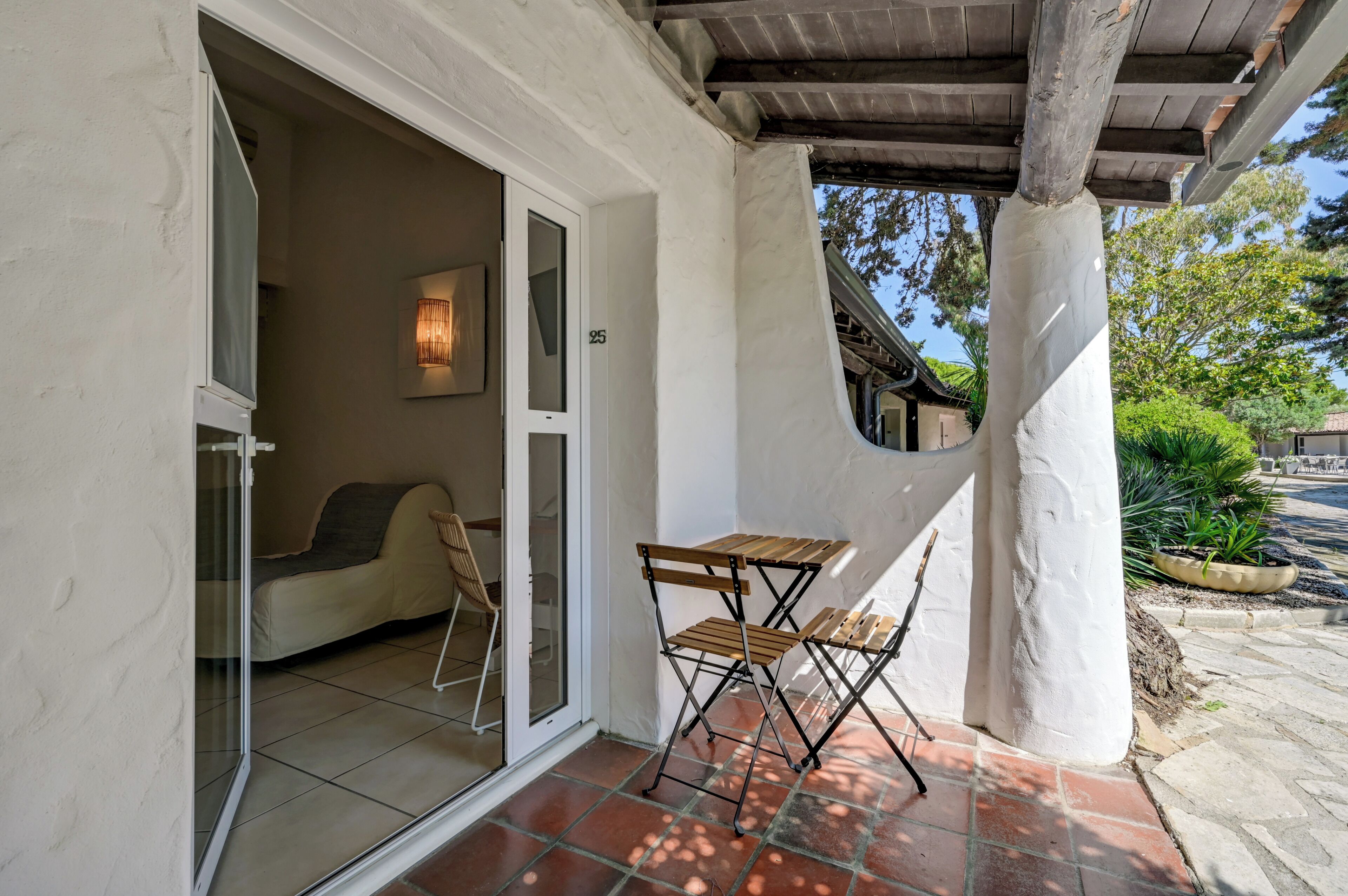 A covered patio area with a table and chairs, a sliding glass door leading to a room, and a number '25' on the wall.
