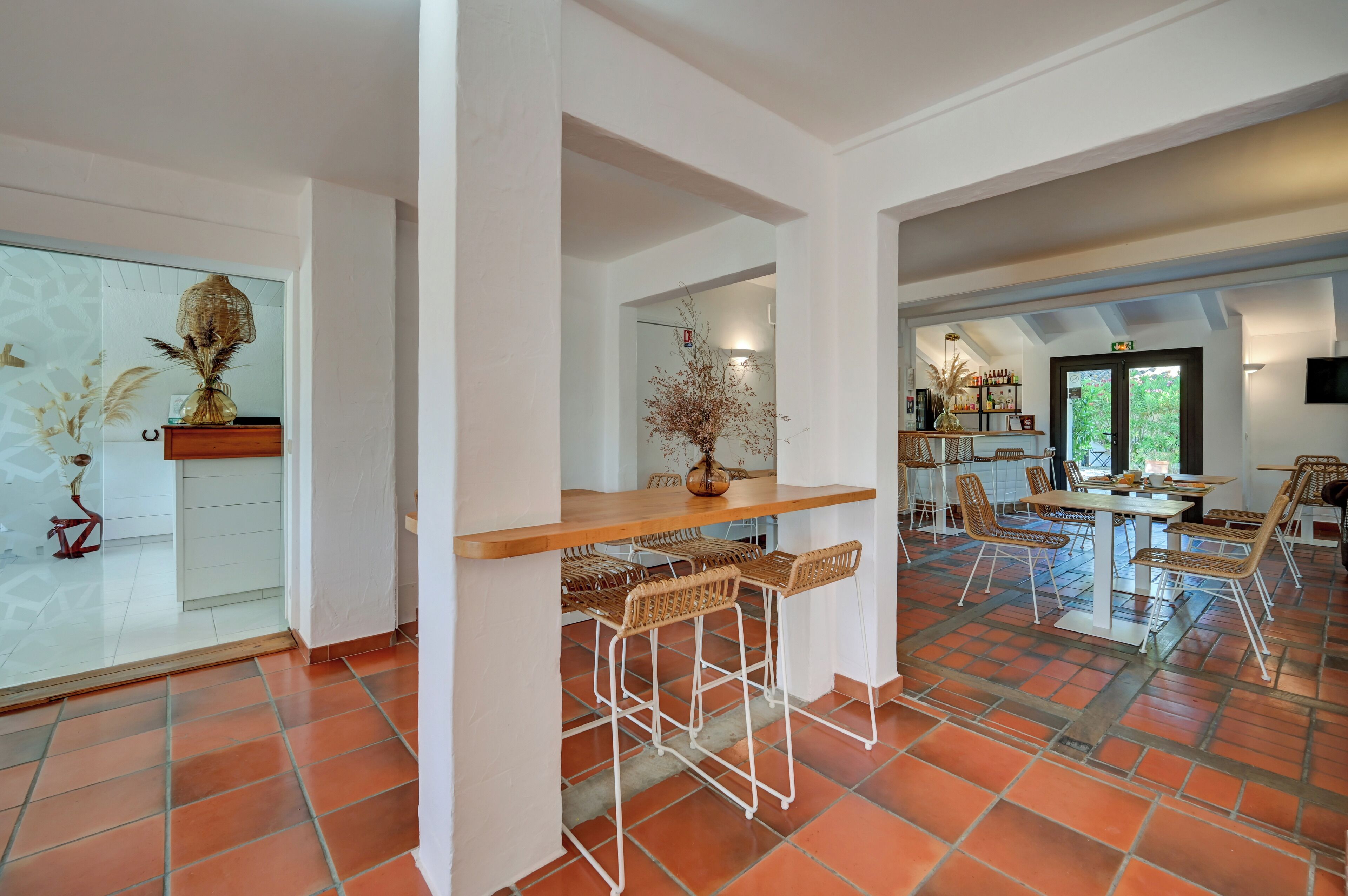 A spacious room with a large window, a wooden table with bar stools, and a decorative vase.