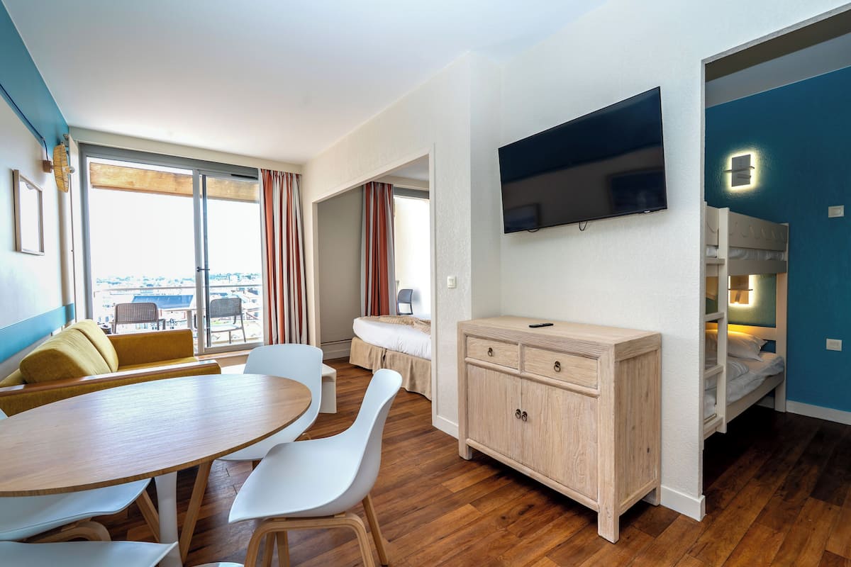 A modern room with a dining table, chairs, a sofa, a TV, and a bed.