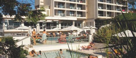 A hotel with a swimming pool, outdoor seating, and a multi-story building with balconies.