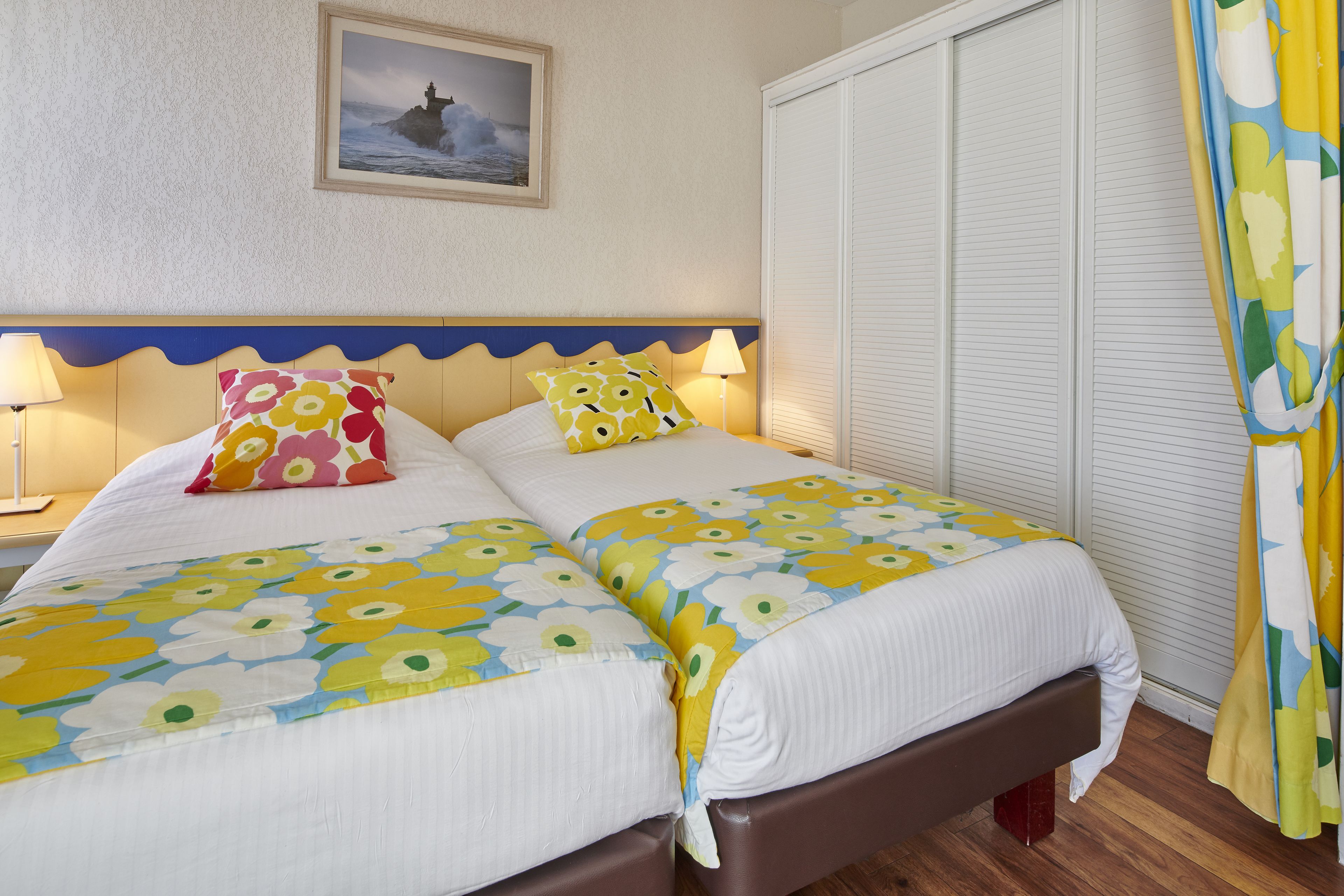A double bed with floral bedding, a nightstand with a lamp, a framed picture on the wall, and a sliding closet door.