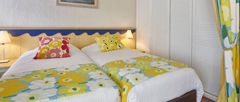 A double bed with floral bedding, a nightstand with a lamp, a framed picture on the wall, and a sliding closet door.