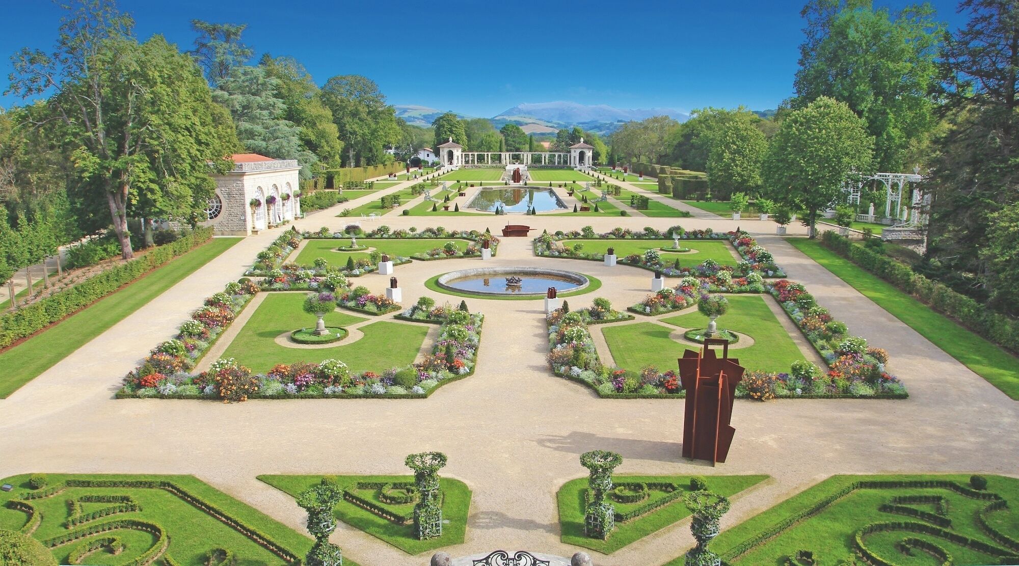 Un jardín formal con senderos simétricos, una fuente central y arquitectura clásica.