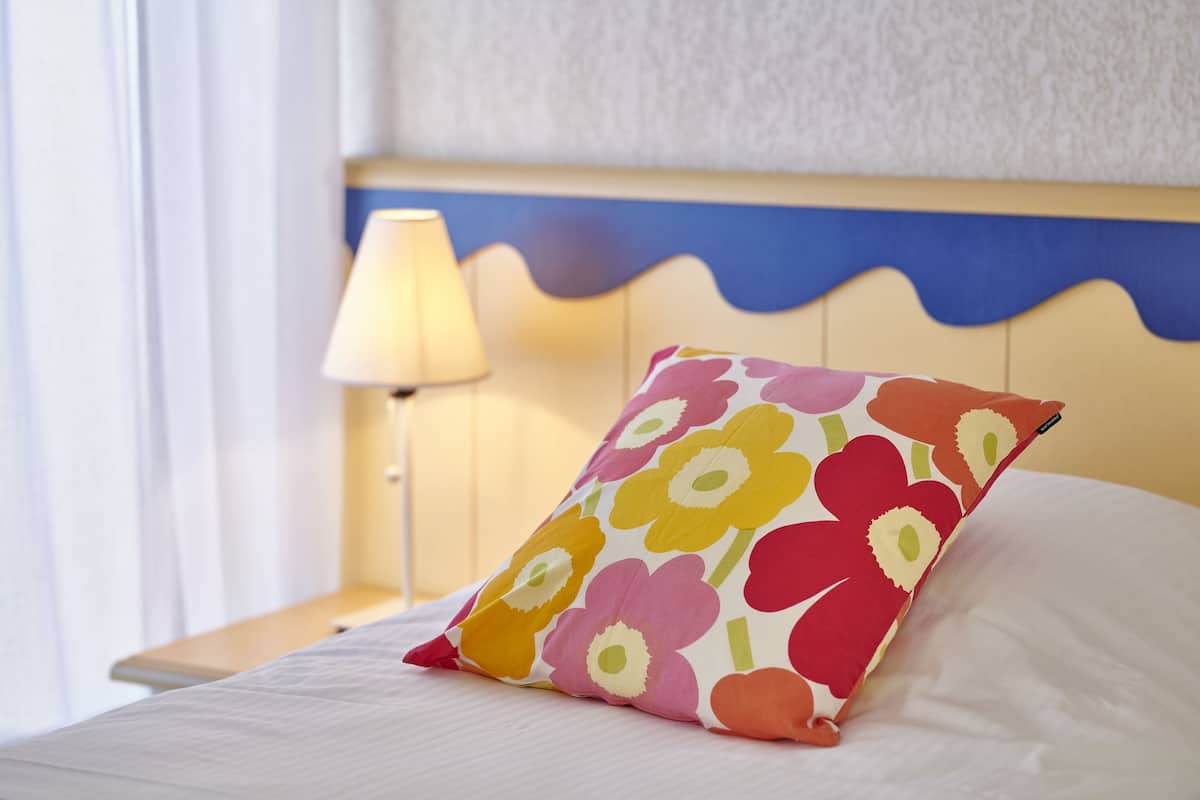 A bed with a colorful floral pillow, a bedside lamp, and a wavy headboard.