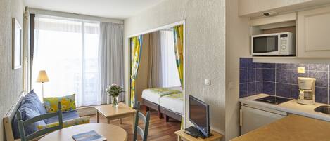 Una habitación de hotel compacta con una cama, una pequeña mesa de comedor, un televisor, un microondas y una kitchenette.