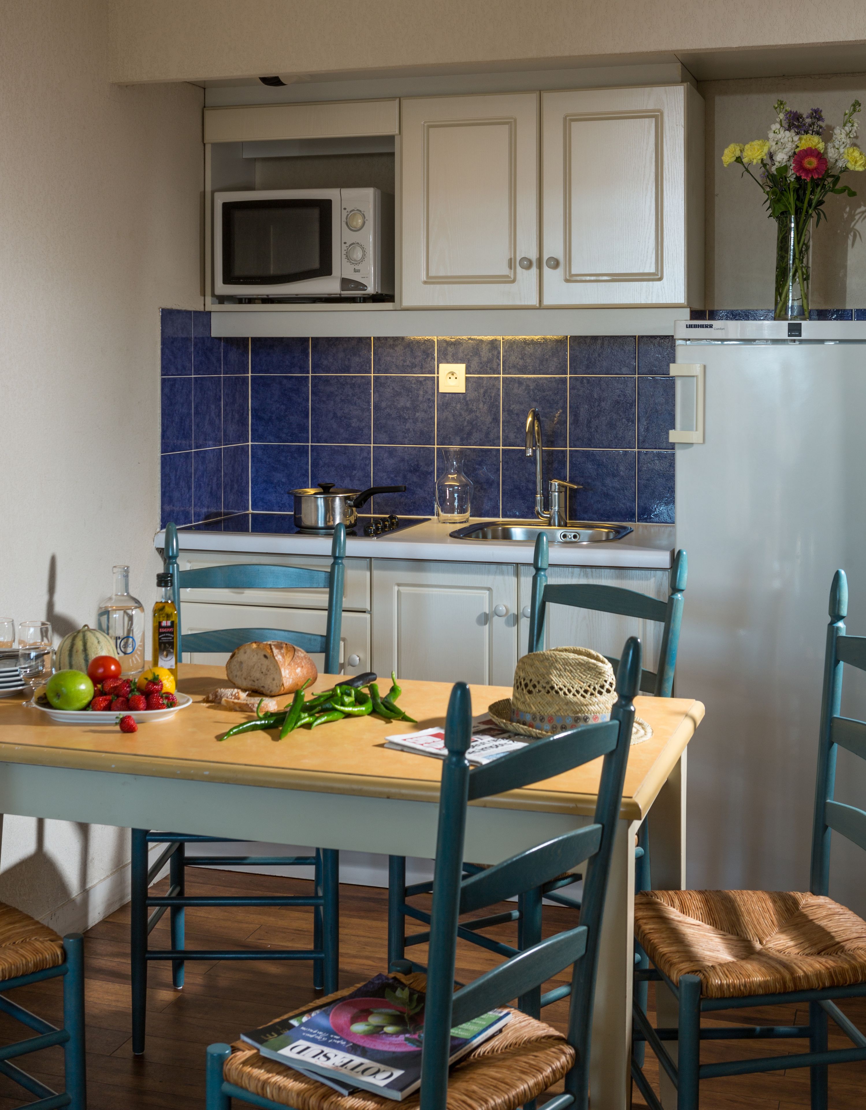 A kitchen with white cabinets, a blue tiled backsplash, a microwave, and a sink.