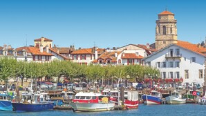 Un port avec des bateaux, une tour et des bâtiments aux toits recouverts de tuiles rouges.