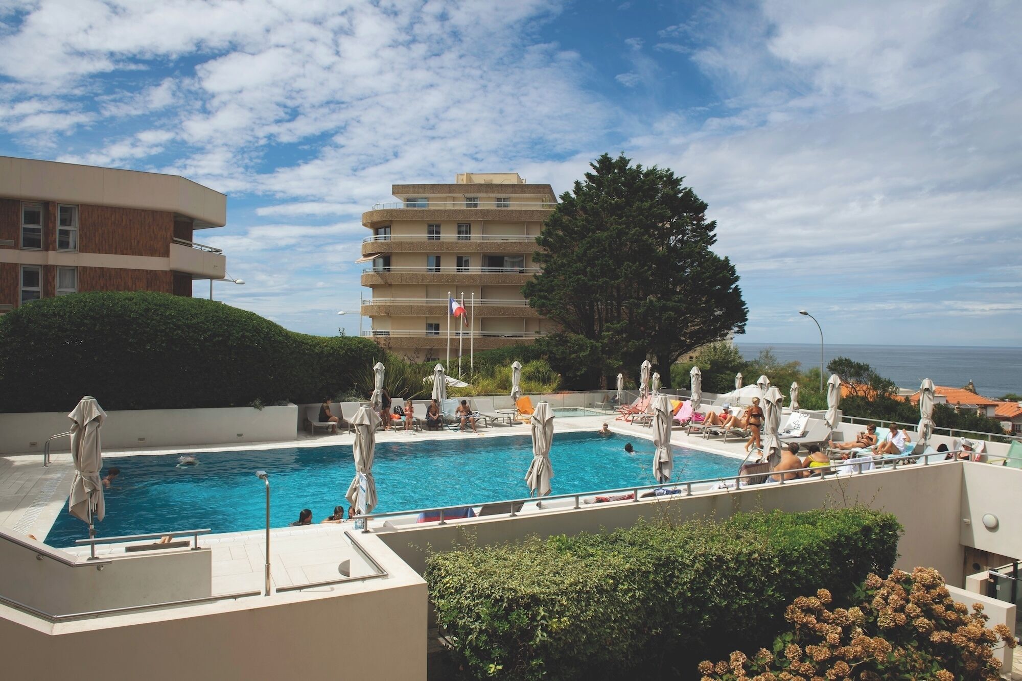 Una piscina al terrat amb múltiples nivells de seients, una bandera i vista al mar.
