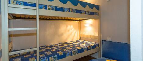 Un lit superposé avec un motif matelassé bleu et blanc, une lampe de chevet et un canapé bleu sur lequel repose un magazine.