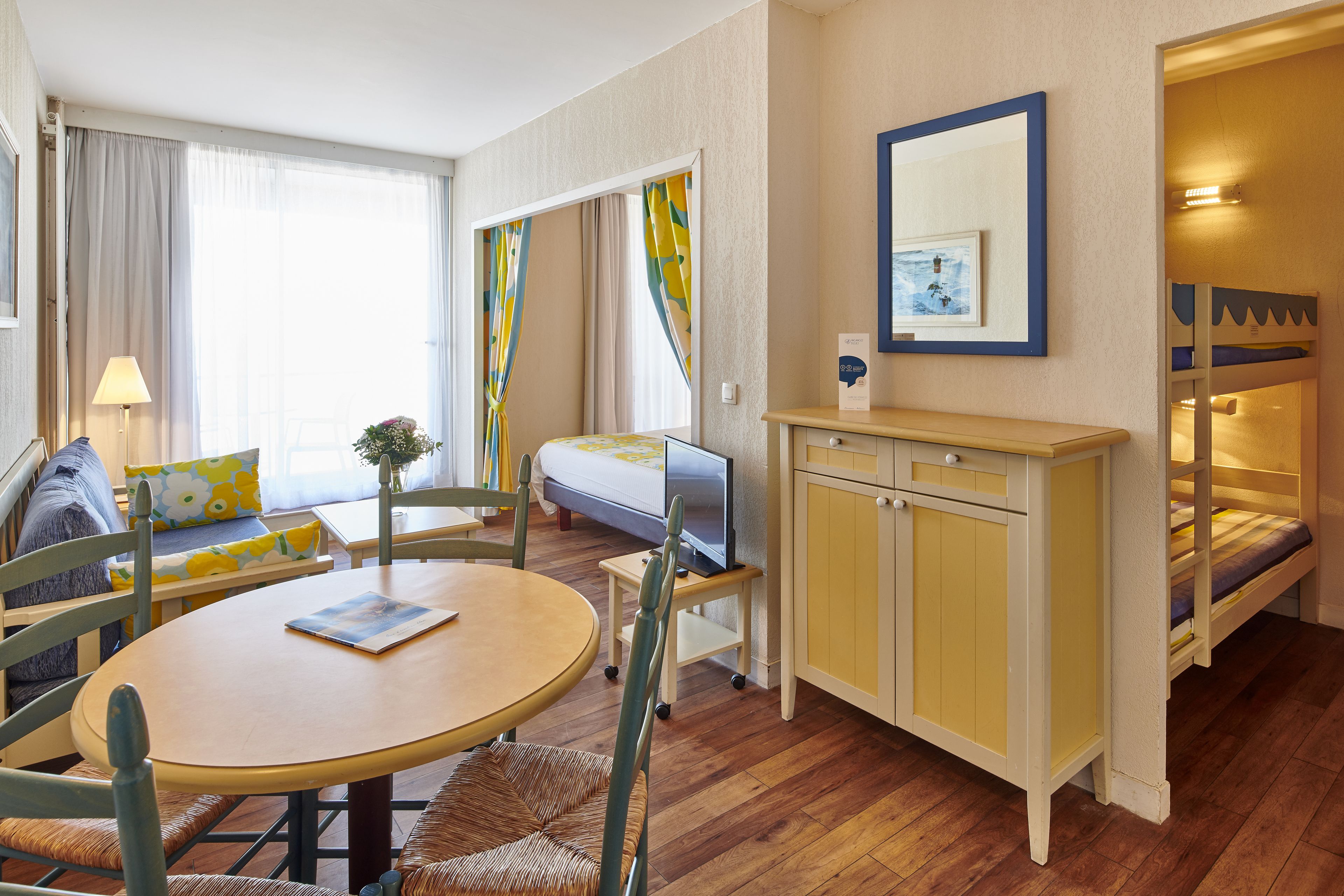 Una habitación acogedora con piso de madera, una mesa redonda con sillas, un sofá, una cama litera y un televisor sobre un pequeño mueble.