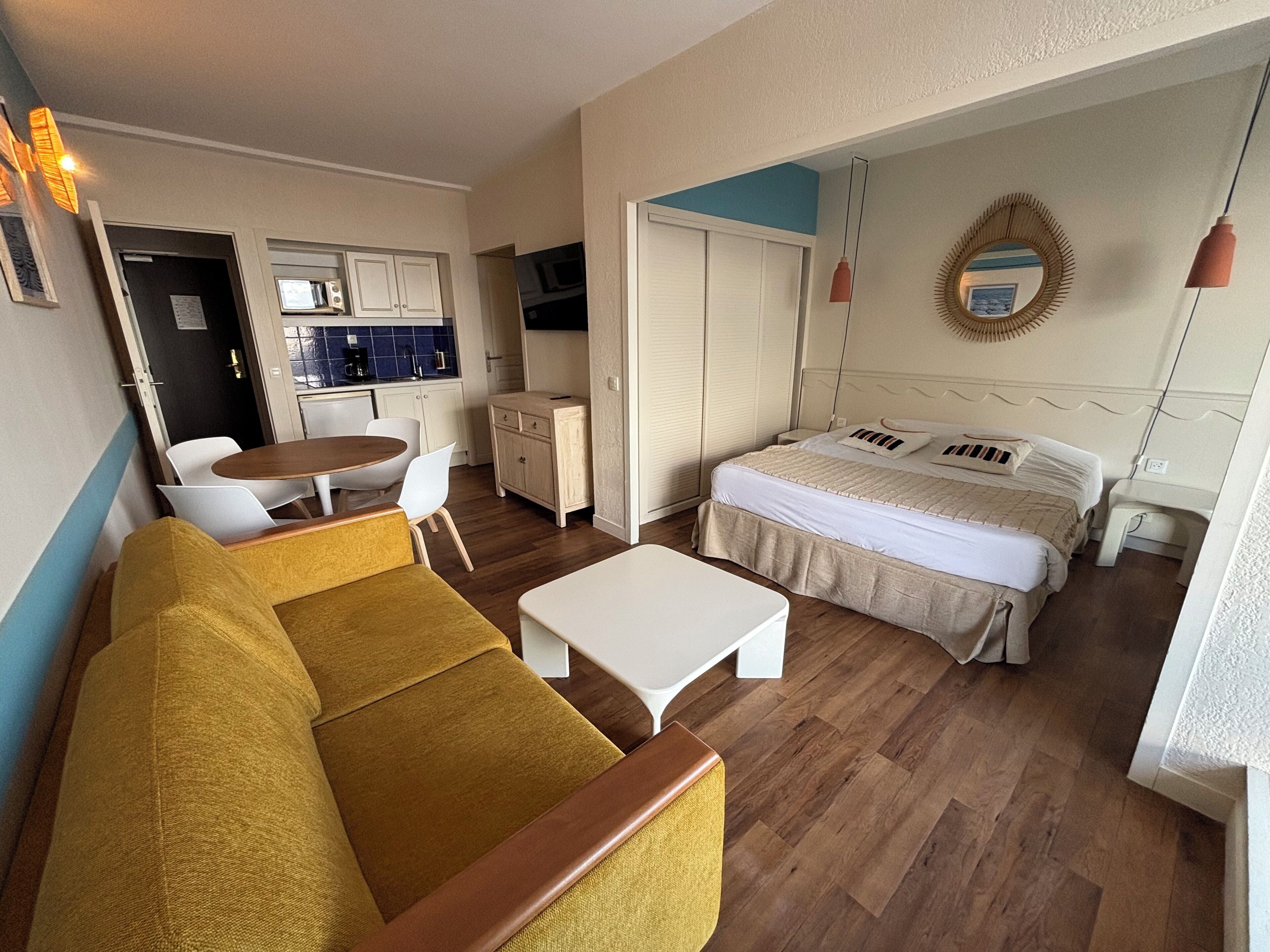 Una habitación de hotel compacta con cama, sofá, pequeña mesa de comedor y kitchenette.