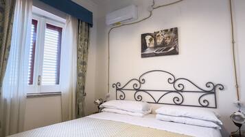 A bedroom with a bed, a window with curtains, an air conditioning unit, a wall-mounted picture, and a hanging light fixture.