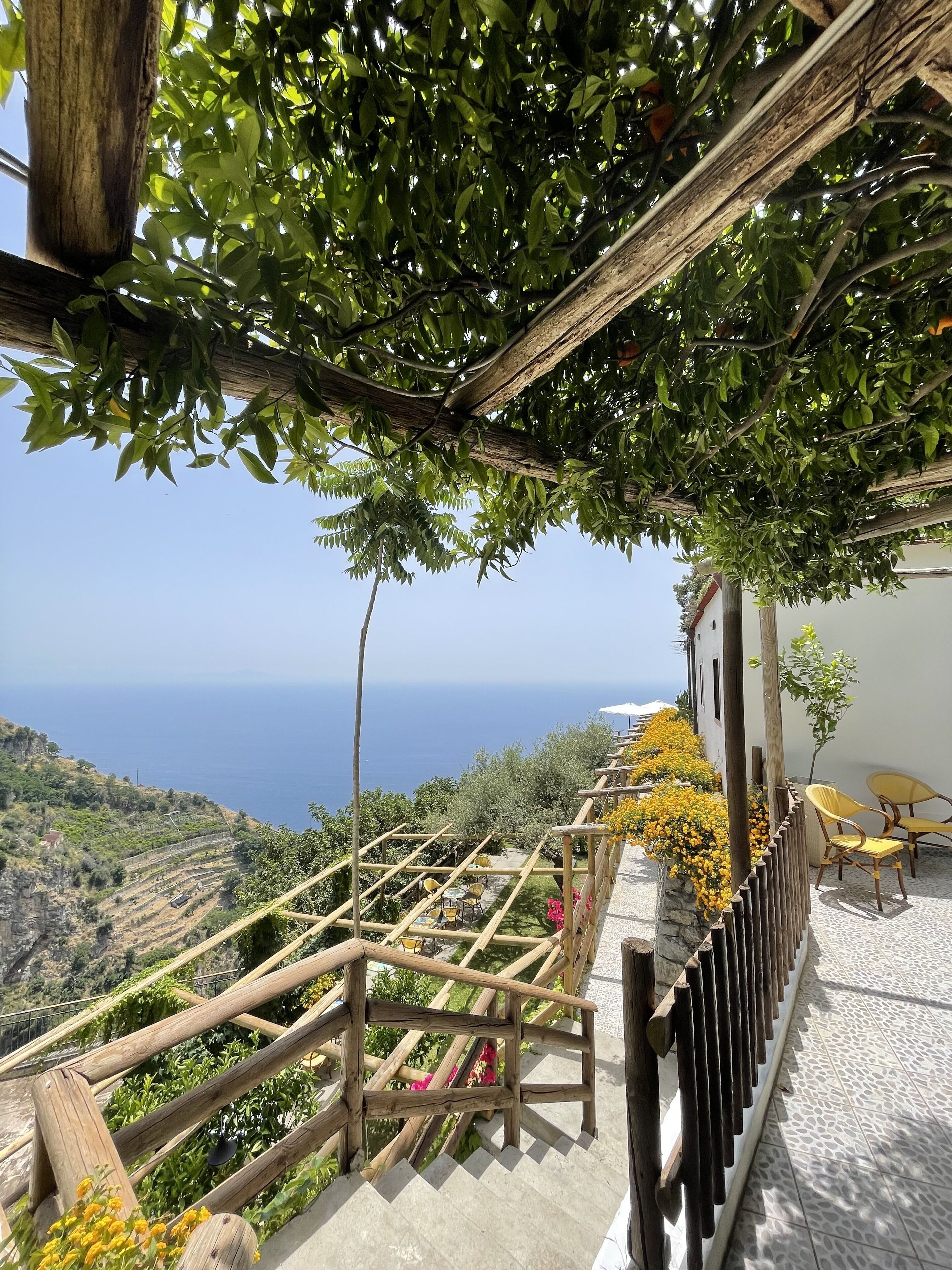 A terrace with a wooden pergola, outdoor seating, and a view of the sea.