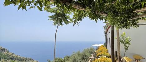 A terrace with a wooden pergola, outdoor seating, and a view of the sea.